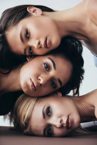 Tres atractivas mujeres jóvenes multiétnicas mirando a la cámara aislada en gris - foto de stock