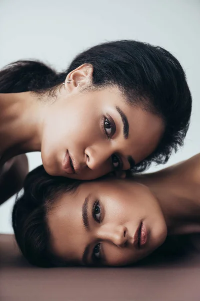 Dos sensuales atractivas mujeres jóvenes multiétnicas mirando a la cámara aislada en gris - foto de stock