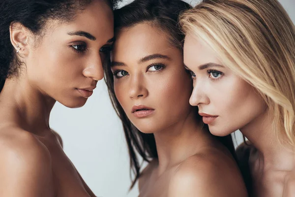 Tres atractivas mujeres jóvenes multiétnicas mirando hacia otro lado aisladas en gris — Stock Photo