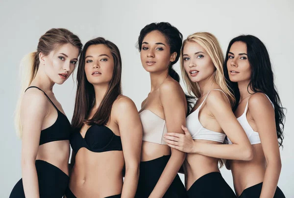 Five sexy multiethnic young women in underwear embracing isolated on grey — Stock Photo