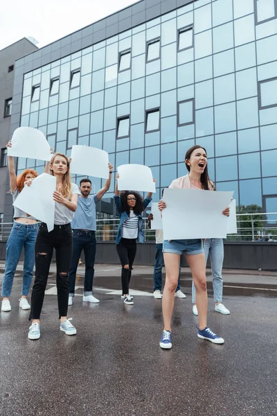 Emotional multicultural people with blank placards near building — Stock Photo
