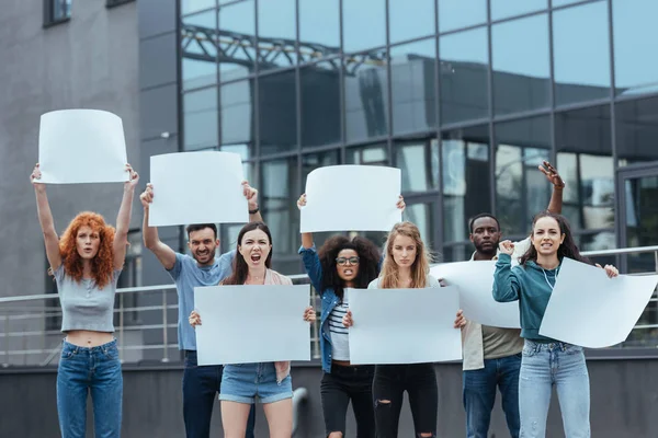 Personas emocionales multiculturales de pie con pancartas en blanco cerca de la construcción - foto de stock