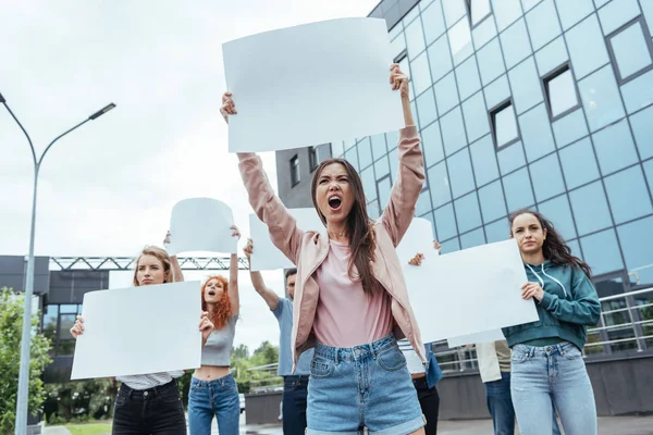Вибірковий фокус емоційної дівчини, що тримає порожній плакат і кричить біля чоловіків і жінок — стокове фото