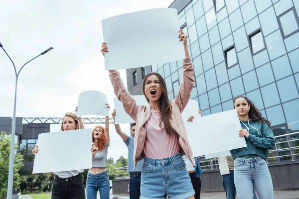 Messa a fuoco selettiva di ragazza emotiva in possesso di cartello bianco e urlando vicino a uomini e donne — Foto stock