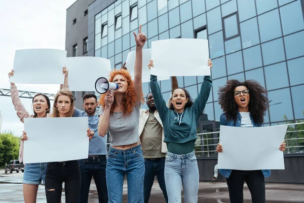 Redhead girl screaming in megaphone near multicultural people — Stock Photo