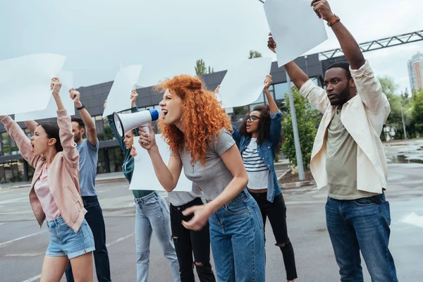 Emotivo rossa ragazza urla in megafono vicino a persone multiculturali — Foto stock