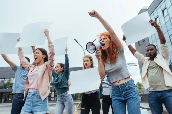 Emotional redhead woman screaming in megaphone near multicultural people — Stock Photo