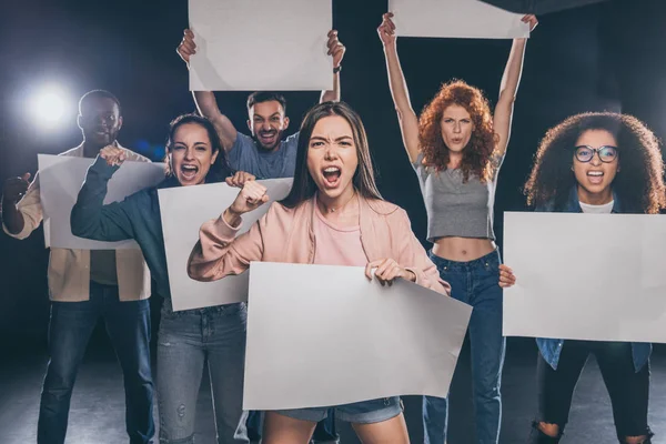 Junge emotionale multikulturelle Menschen schreien, während sie leere Plakate auf schwarz halten — Stockfoto