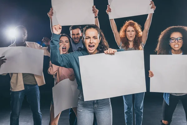 Emotional multicultural people screaming while holding blank placards on black — Stock Photo