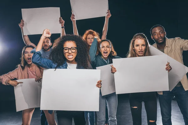 Jeunes personnes multiculturelles criant tout en tenant des pancartes vierges sur noir — Photo de stock