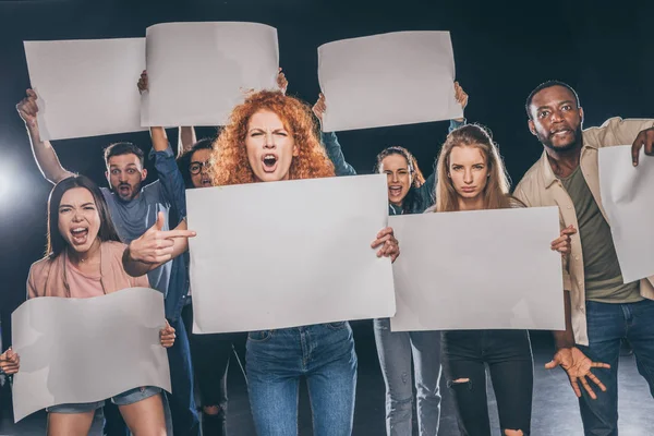 Jóvenes multiculturales gritando mientras sostienen tablas vacías en negro - foto de stock