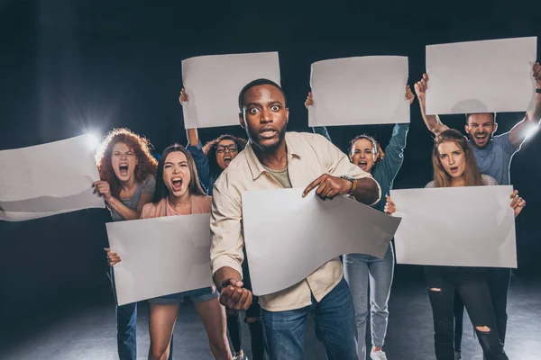 Selective focus of shocked african american man near people with blank placards on black — Stock Photo