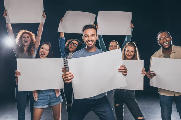 Positive multicultural people screaming while holding blank placards on black — Stock Photo