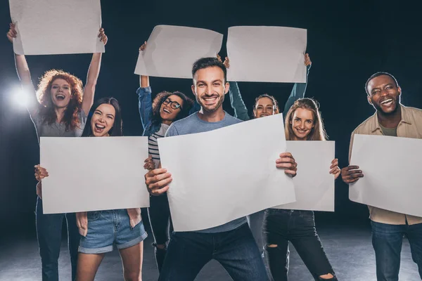 Personnes multiculturelles positives criant tout en tenant des pancartes vierges sur noir — Photo de stock