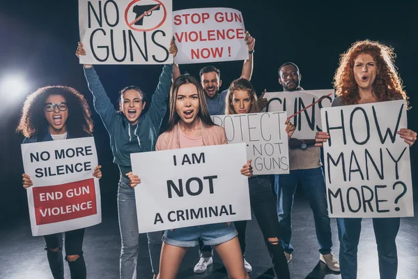 Emotional multicultural people screaming while holding placards on black — Stock Photo