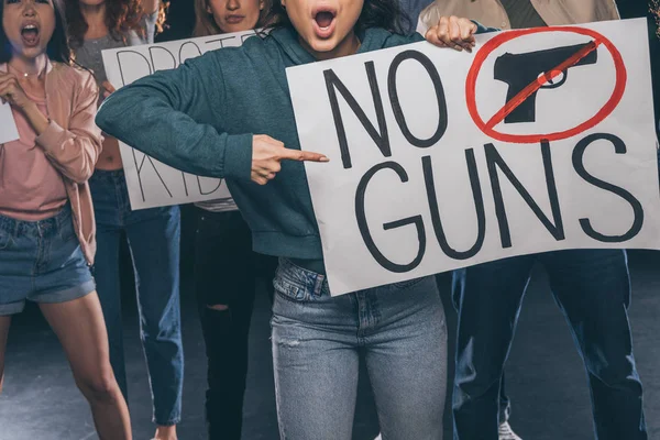 Foyer sélectif de la fille pointant avec le doigt à la plaque sans lettrage pistolet près des gens sur noir — Photo de stock