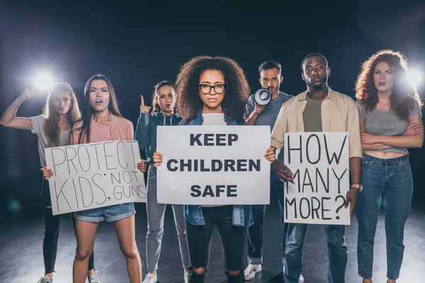 African american woman holding placard with keep children safe lettering near group of people on black — Stock Photo