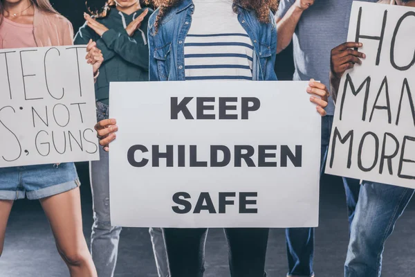 Vista cortada da mulher segurando cartaz com manter as crianças letras seguras perto do grupo de pessoas em preto — Fotografia de Stock
