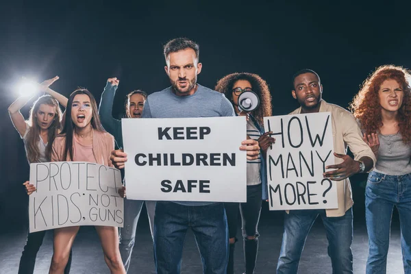 Uomo arrabbiato tenendo cartello con tenere i bambini lettering sicuro vicino a persone multiculturali su nero — Stock Photo