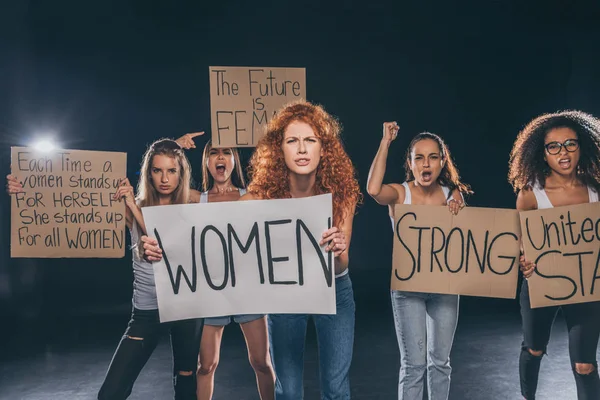 Femmes multiculturelles émotionnelles debout et tenant des pancartes sur noir — Photo de stock