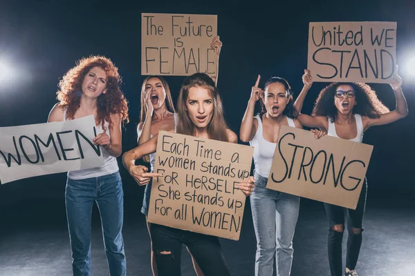 Atractivas mujeres multiculturales gritando y sosteniendo pancartas en negro - foto de stock