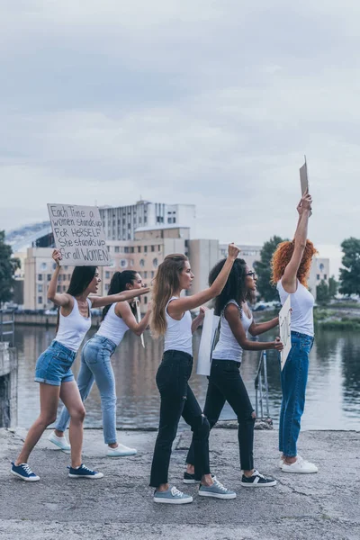 Filles multiculturelles tenant des pancartes et criant tout en marchant dehors — Photo de stock