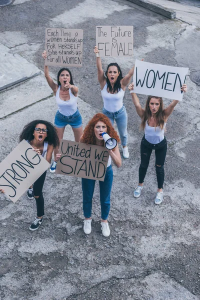 Vista aérea de chicas emocionales multiculturales sosteniendo pancartas y gritando afuera — Stock Photo