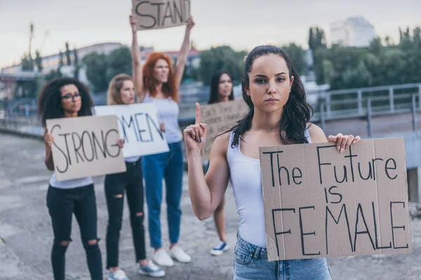 Selective focus of attractive girl pointing with finger while holding placard with the future is female letters — Stock Photo