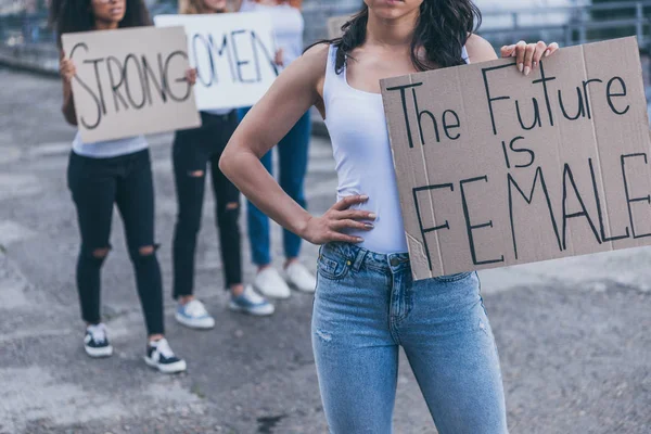 Vista recortada de niña sosteniendo pancarta con el futuro es letras femeninas, mientras que de pie con la mano en la cadera - foto de stock