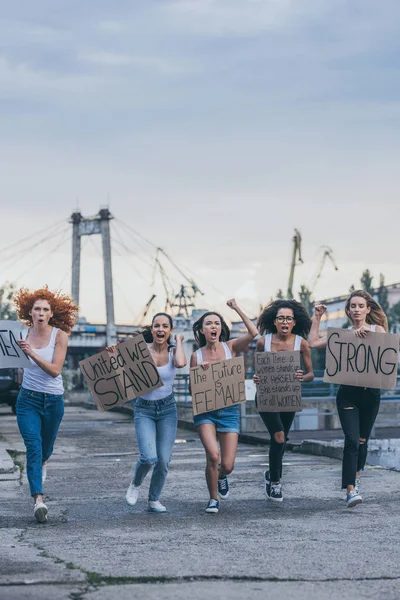 Mujeres multiculturales sosteniendo pancartas y corriendo afuera - foto de stock