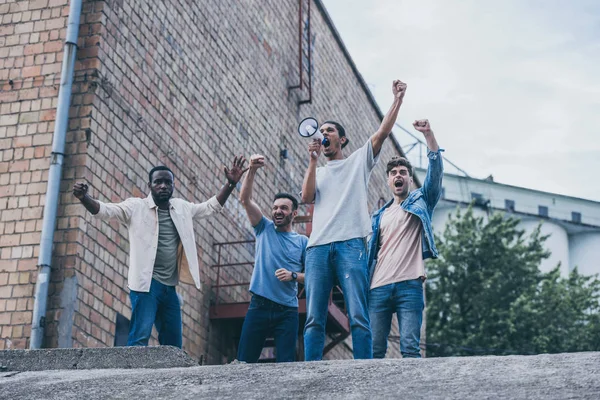 Hombre emocional gritando en megáfono cerca de personas multiculturales fuera - foto de stock