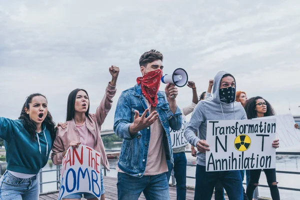 Hombres con bufandas en las caras gestos cerca de personas multiculturales con pancartas - foto de stock