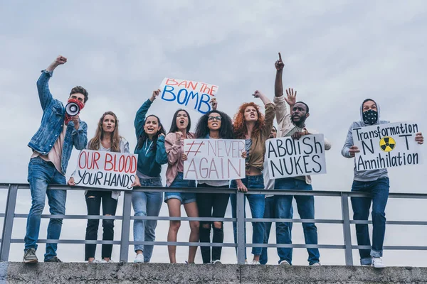 Hombre con bufanda en el gesto de la cara mientras grita en megáfono cerca de personas multiculturales con letras en carteles - foto de stock