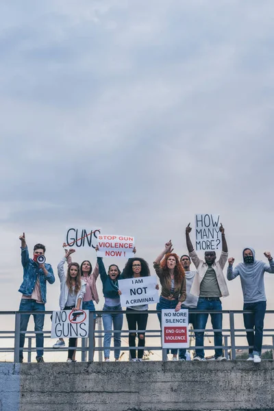 Man with scarf on face screaming in megaphone near multicultural people with lettering on placards — Stock Photo