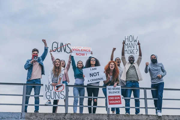 Mann mit Schal im Gesicht schreit in Megafon neben multikulturellen Menschen mit Schriftzügen auf Plakaten, die draußen gestikulieren — Stockfoto