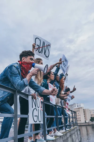 Emotional man with scarf on face gesturing and holding megaphone near multicultural people with placards — Stock Photo