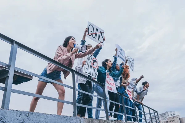 Vista basso angolo di donna con megafono urlando con gruppo di persone multiculturali che tengono cartelli — Foto stock