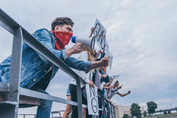 Людина з шарфом на обличчі жестикулює і тримає мегафон біля мультикультурних людей з плакатами — стокове фото