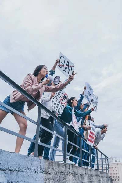 Низкий угол обзора девушки с мегафоном кричит с группой мультикультурных людей, держащих плакаты — стоковое фото