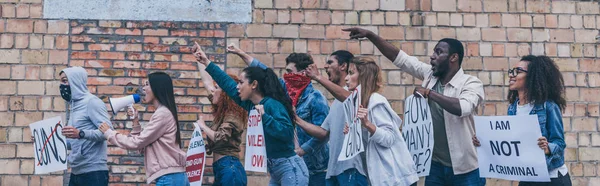 Prise de vue panoramique de personnes multiculturelles marchant près d'un mur de briques pendant une manifestation — Photo de stock