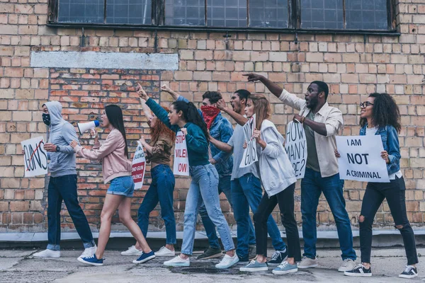 Personas multiculturales caminando cerca de la pared de ladrillo durante la protesta - foto de stock