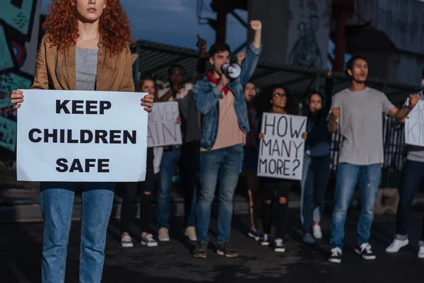 Vue recadrée de rousse fille tenant une pancarte avec garder les enfants lettrage sûr près de personnes multiculturelles sur la réunion — Photo de stock