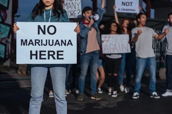 Обрезанный вид женщины с плакатом без надписей от марихуаны рядом с кричащими мультикультурными людьми — стоковое фото