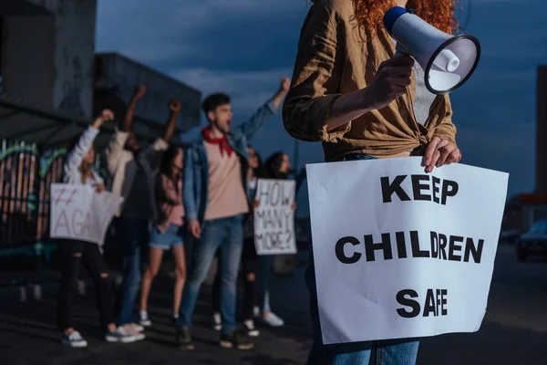 Vista cortada da menina segurando cartaz com manter as crianças letras seguras perto de pessoas multiculturais na reunião — Fotografia de Stock