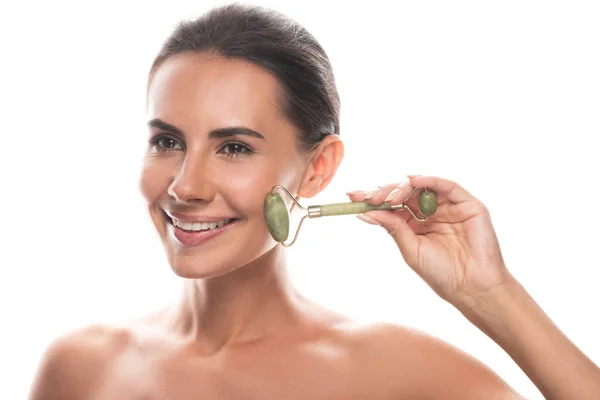 Naked young woman using facial jade roller and smiling isolated on white — Stock Photo