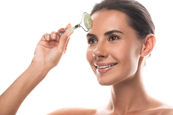 Mujer joven desnuda usando rodillo de jade facial y sonriendo aislado en blanco — Stock Photo