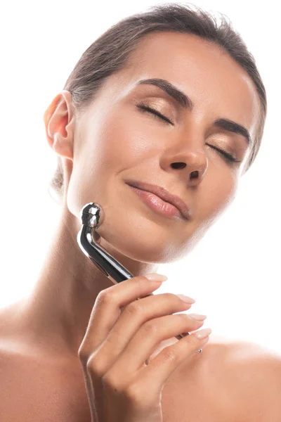 Naked young woman using facial massager with closed eyes isolated on white — Stock Photo