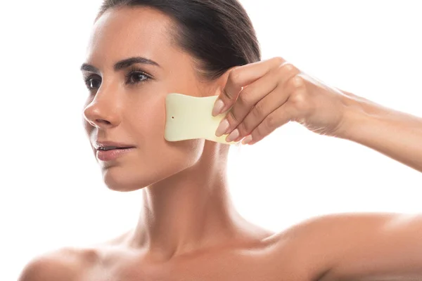 Nude young woman using gua sha scraper isolated on white — Stock Photo