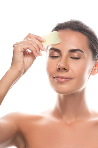 Nude young woman using gua sha scraper with closed eyes isolated on white — Stock Photo