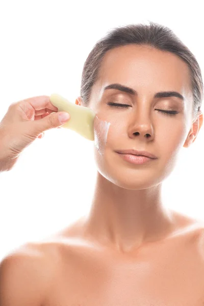 Vue partielle du cosmétologue appliquant la crème pour le visage et utilisant gua sha grattoir isolé sur blanc — Photo de stock